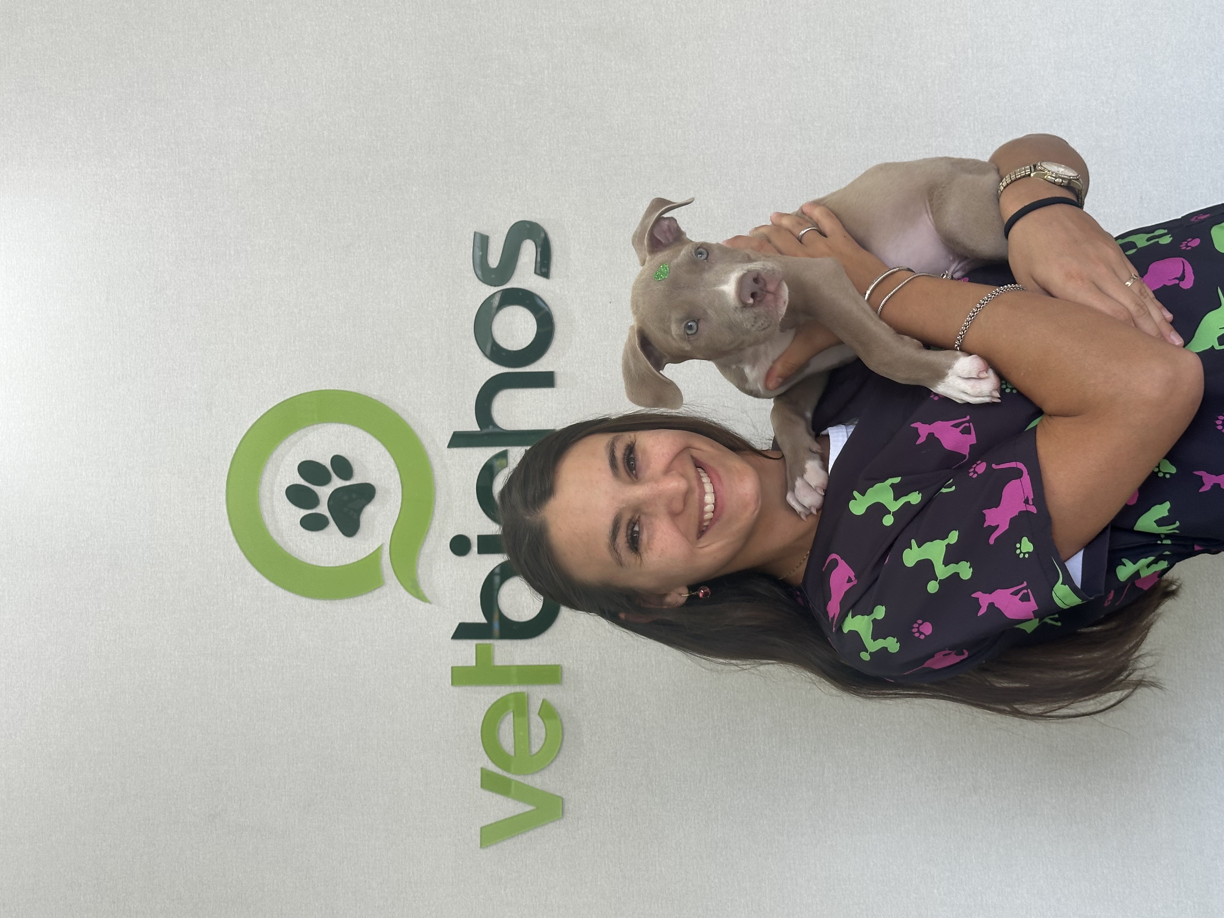 Veterinária da Vetbichos com cachorro em frente ao logo da clínica em Itapema-SC